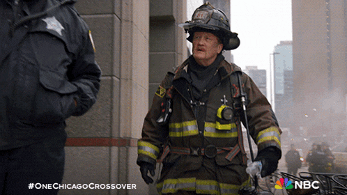 a man in a fireman 's uniform stands next to a police officer with the hashtag #onechicagocrossover on the bottom
