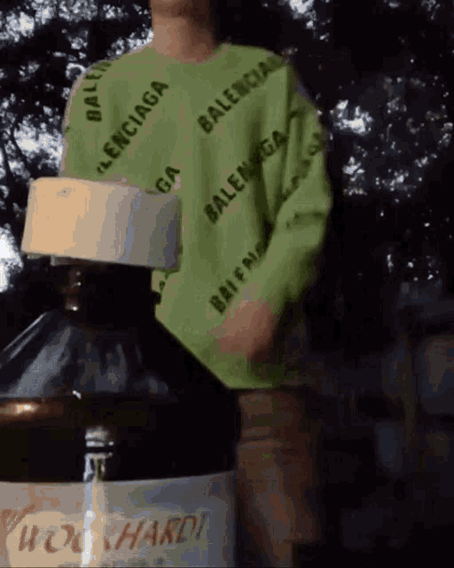 a person wearing a green balenciaga sweater is standing next to a large bottle of whiskey .