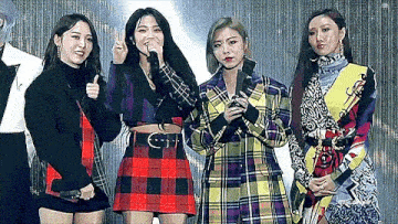 a group of four women are standing next to each other on a stage .