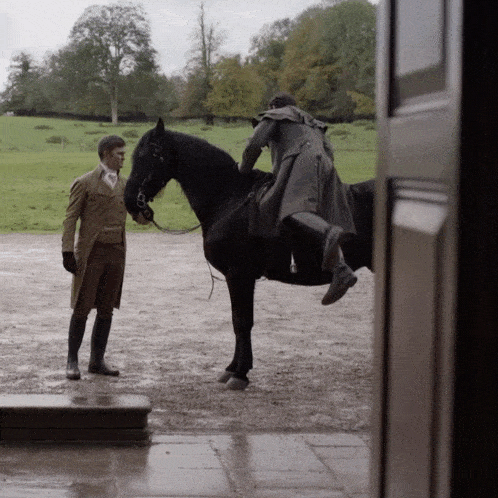 a man standing next to a black horse while another man rides it