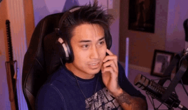 a man wearing headphones is sitting in front of a microphone and talking on a cell phone .