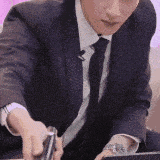 a man in a suit and tie is sitting at a table holding a pen and a microphone .