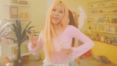 a woman in a pink top and blue shorts stands in front of a yellow wall