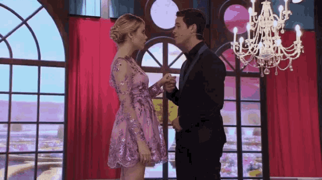 a man in a suit and a woman in a purple dress are dancing in a room with a chandelier