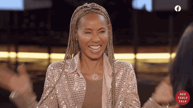 a woman wearing a sequined jacket is smiling in front of a red table talk sign