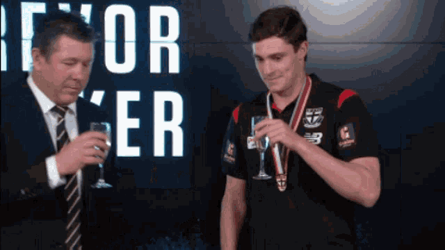 a man in a suit and tie stands next to a man in a medal holding a glass of wine