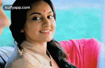 a woman with a red dot on her forehead is smiling in front of a body of water .