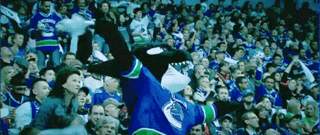 a mascot in a vancouver canucks jersey is dancing in front of a crowd .