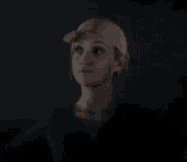 a woman wearing a baseball cap is standing in the dark looking up .