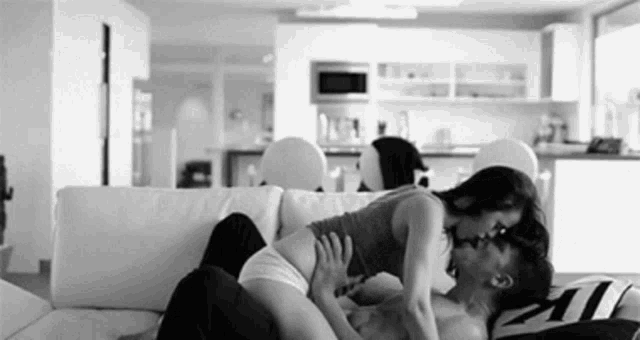 a man and a woman are kissing on a couch in a black and white photo .