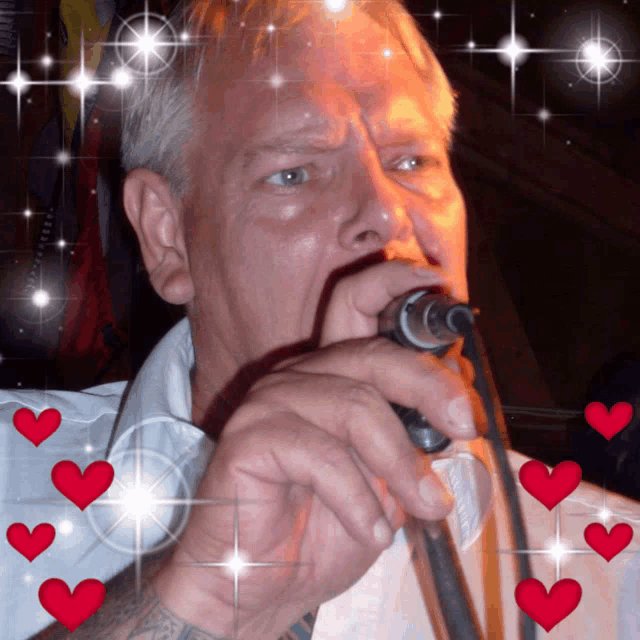 a man is singing into a microphone with red hearts around him