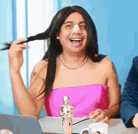 a woman in a pink dress is sitting at a table with a statue of an oscar winner in front of her