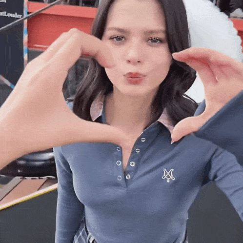 a woman wearing a blue shirt with the letter x on it makes a heart shape with her hands