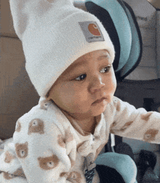 a baby wearing a white carhartt hat looks at the camera
