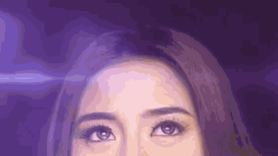 a close up of a woman 's eyes with a purple light behind them .