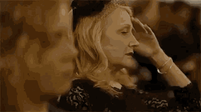 two women are sitting next to each other in a room . one of the women is holding her hand to her forehead .