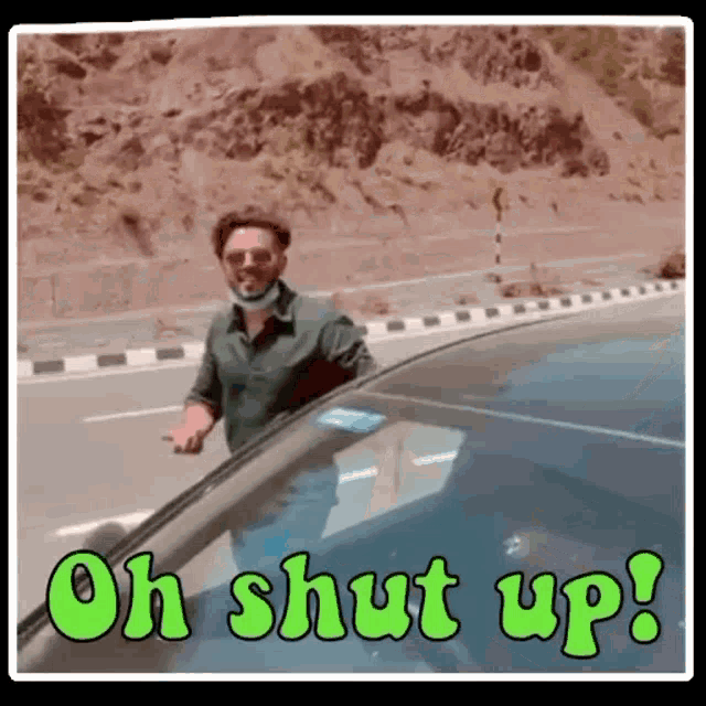 a man in a mask is standing next to a car with the words oh shut up written on it .