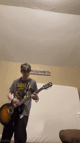 a man wearing a nirvana shirt plays a guitar