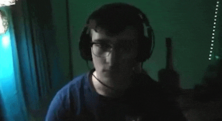 a man wearing headphones and glasses is holding a gun in his hand in a dark room .