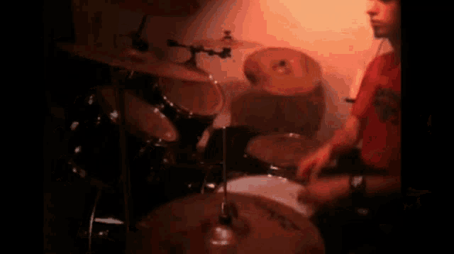 a man in a red shirt playing drums in a dark room