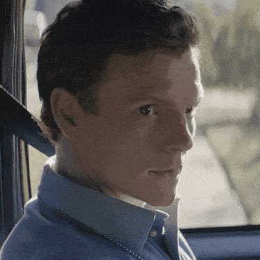 a man in a blue shirt is looking out of a car window