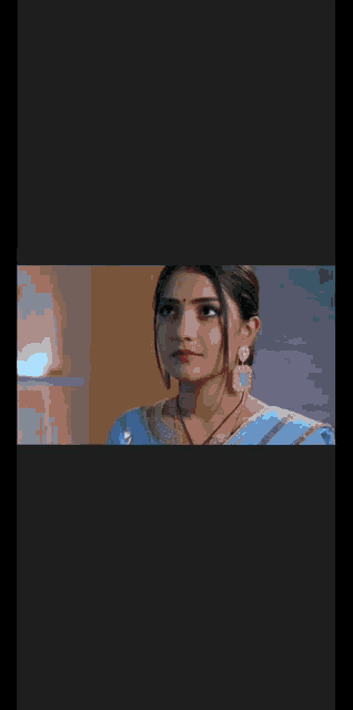 a woman is wearing a blue saree and earrings and looking up .