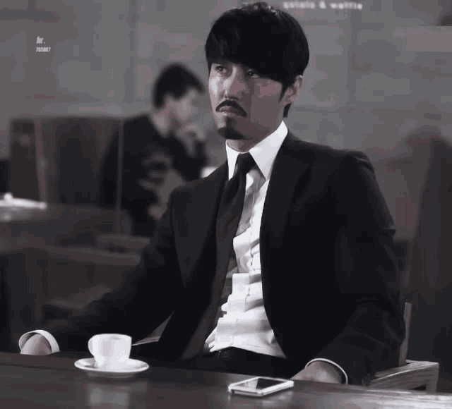 a man in a suit is sitting at a table with a cup of coffee