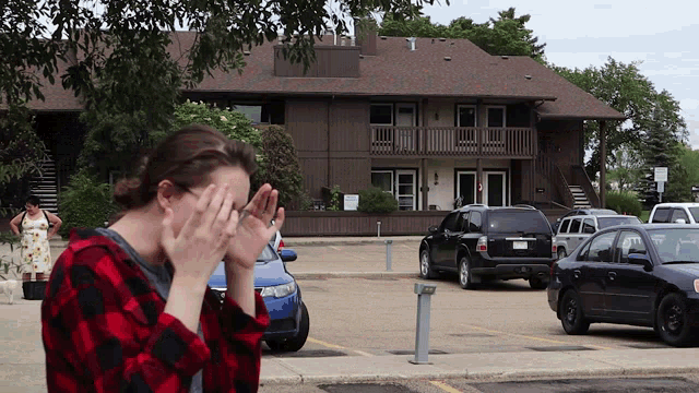 a woman covering her face with her hands in front of a parking lot