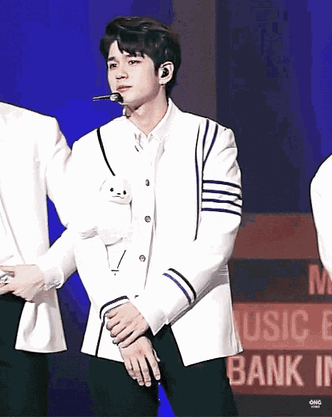 a man in a white jacket is holding a teddy bear in his pocket while standing on a stage .