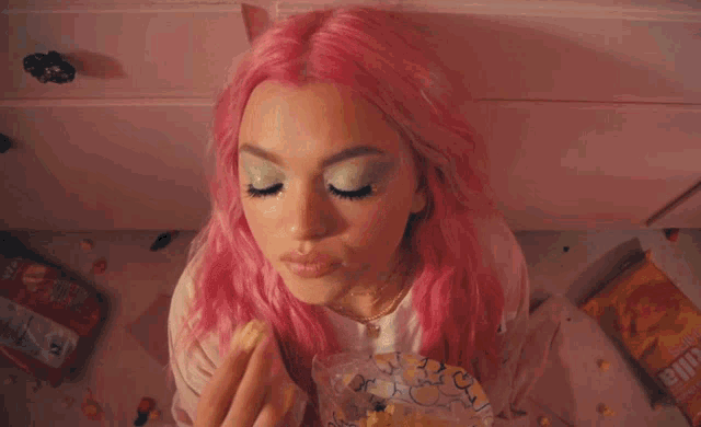 a woman with pink hair is holding a bag of popcorn and looking up