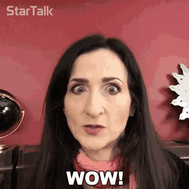 a woman is making a surprised face and says wow in front of a red wall