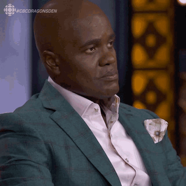 a man in a green suit is sitting in front of a cbs dragonsden logo