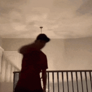 a man in a red shirt is standing on a staircase with a ceiling fan hanging from the ceiling .