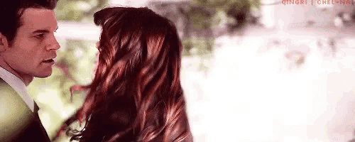 a man and a woman are standing next to each other and kissing . the woman has red hair .