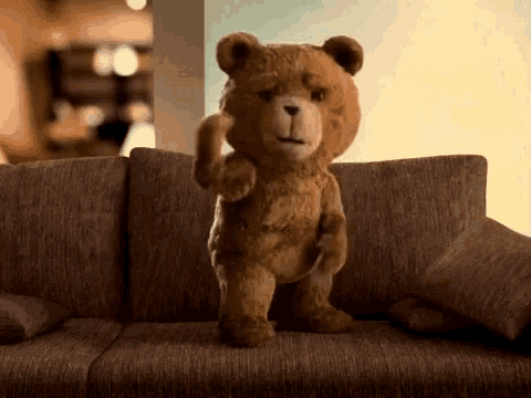a teddy bear is standing on a couch and talking on a cell phone .