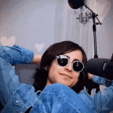 a man wearing sunglasses and a denim jacket is sitting in front of a microphone .