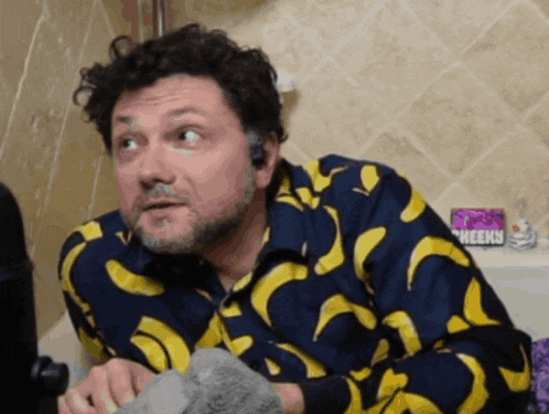 a man wearing a blue shirt with yellow bananas on it looks surprised