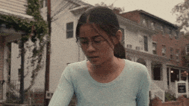 a young woman wearing glasses and a blue shirt stands in front of a row of houses