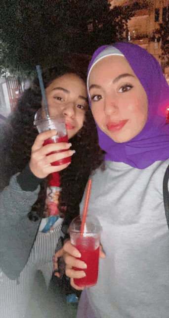 a woman in a purple head scarf holds a cup of red liquid next to another woman