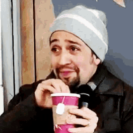 a man wearing a beanie is holding a cup of coffee and a cup of tea .
