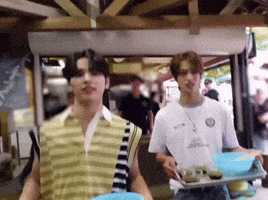 two men are standing next to each other in a room holding trays of food .