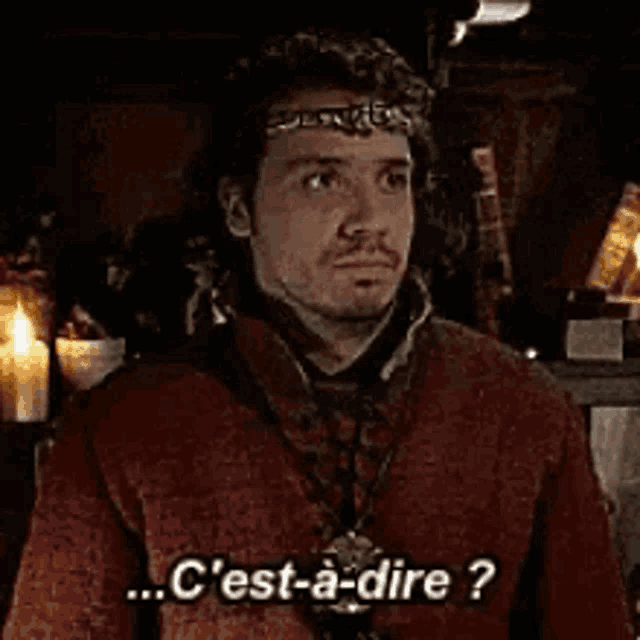 a man in a red jacket and a crown is talking in a dark room .