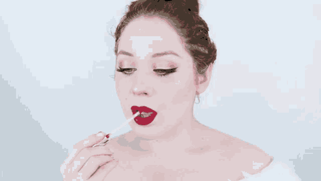 a woman is applying red lipstick with a brush .