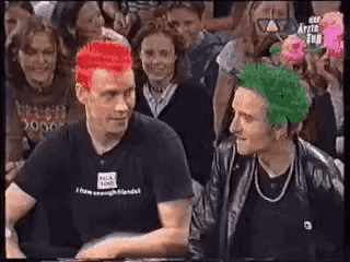 two men with green and red hair are standing next to each other in front of a crowd .