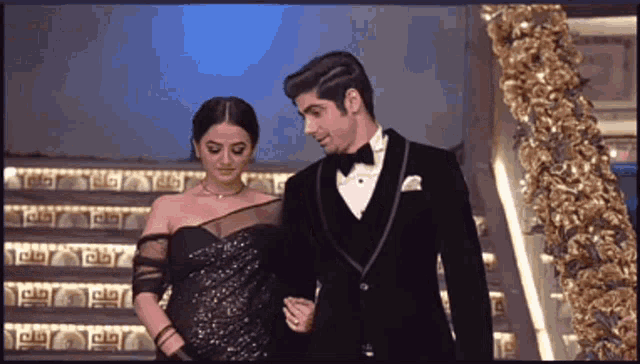 a man in a tuxedo and a woman in a black dress walk down stairs