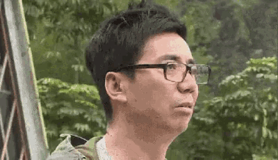 a man wearing glasses is making a funny face while standing in front of trees .