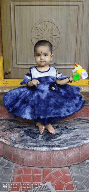 a baby in a blue dress is standing in front of a door