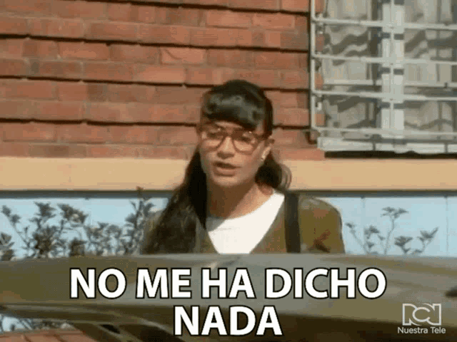 a woman with glasses says no me ha dicho nada in front of a brick wall