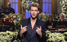 a man in a suit is giving a thumbs up sign in front of flowers .