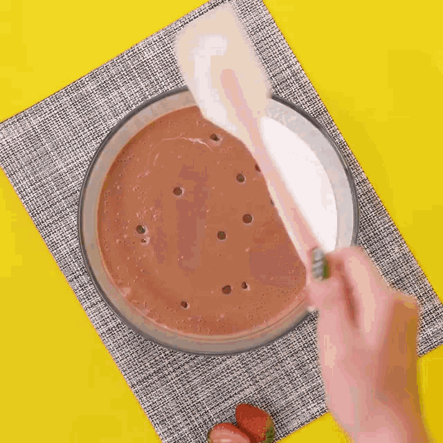 a person is stirring a bowl of chocolate and milk with a wooden spoon